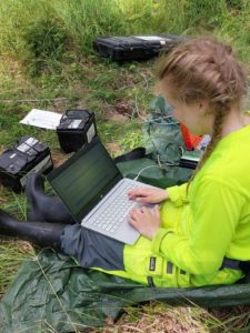 Geologinainen istuu nurmella tietokone sylissään