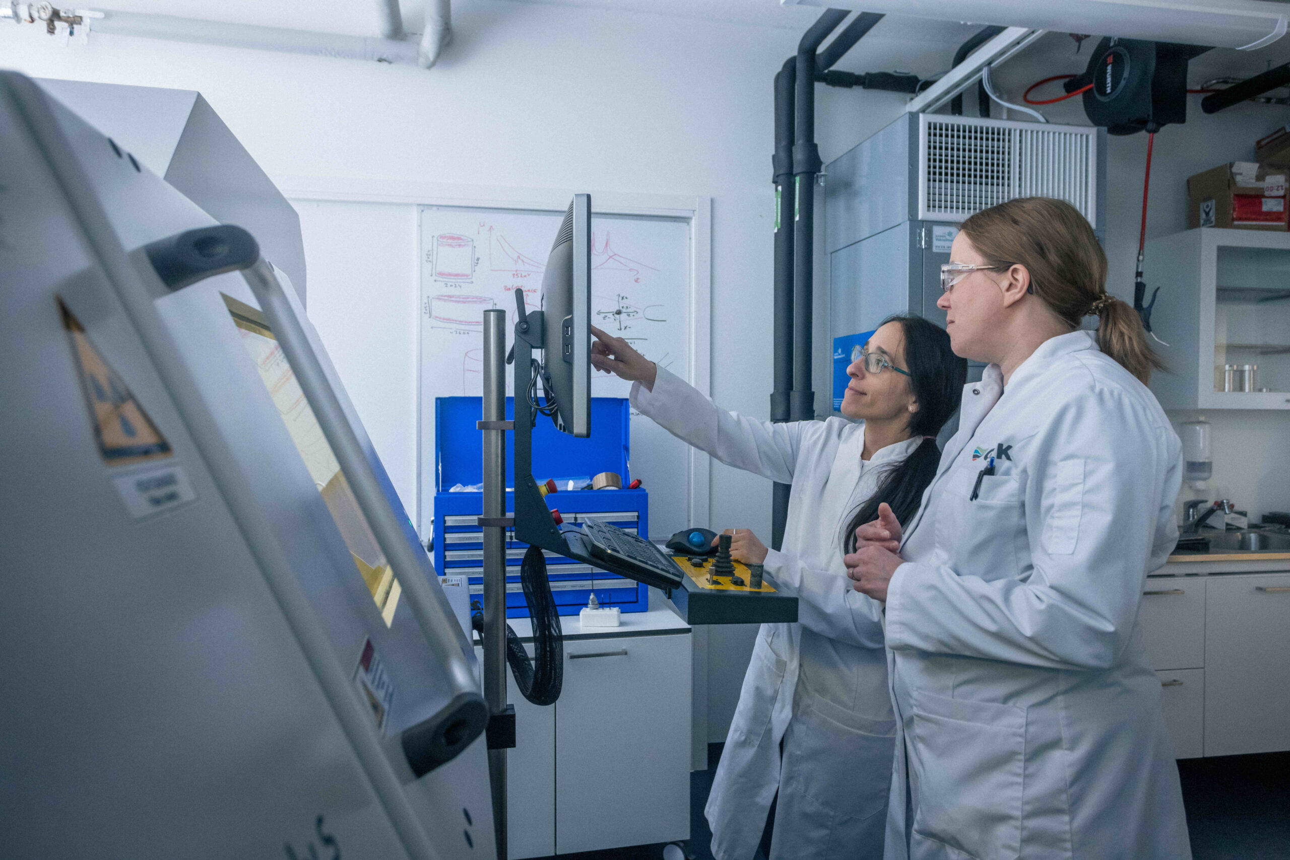 Kaksi henkilöä labratakeissa laboratoriossa tutkailemassa tutkimuslaitteen näyttöä