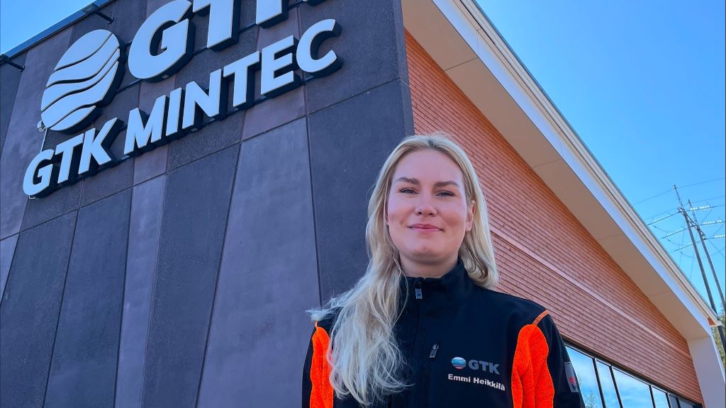 Nainen katsoo hymyillen kameraan, taustalla GTK Mintec.