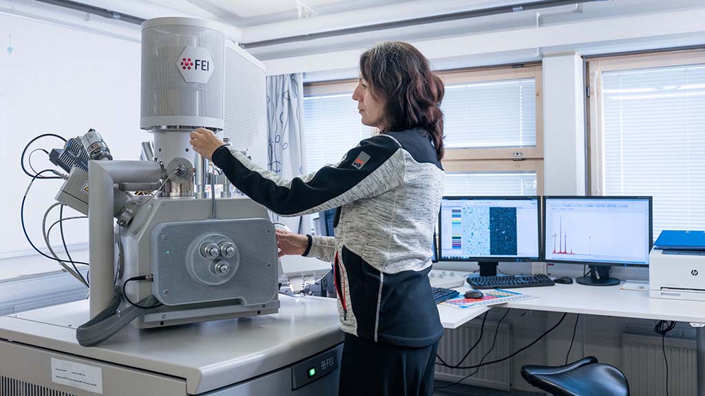 Henkilö käyttää laboratoriolaitetta, jonka vieressä on kaksi tietokonenäyttöä, joissa näkyy analyysituloksia.