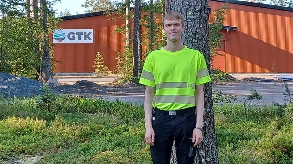 Henkilö keltaisessa huomiopaidassa seisoo GTK-logollisen, punaisen rakennuksen edessä.