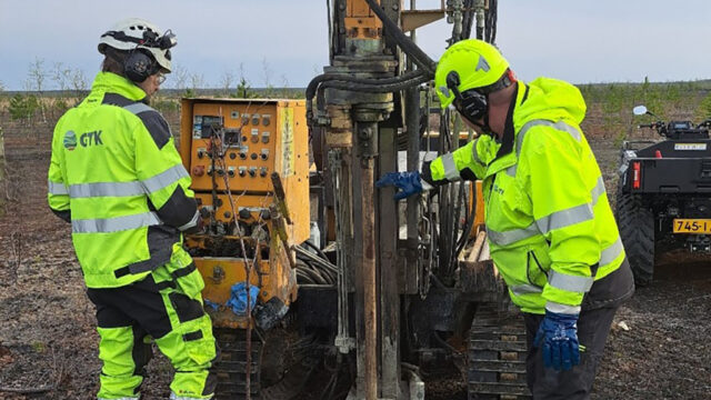 Two people are working at a drilling machine outdoors.