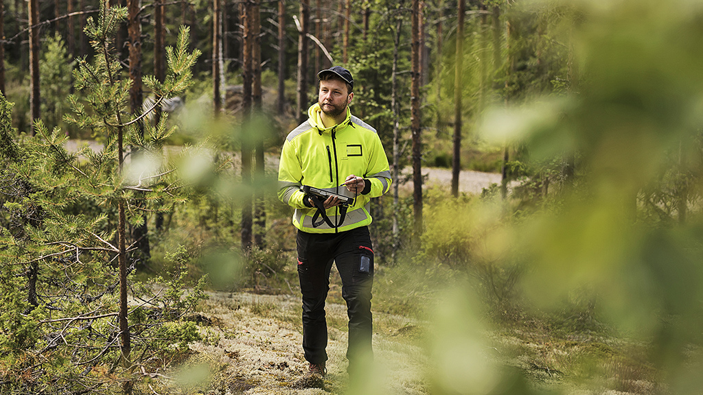Huomioasuun pukeutunut henkilö merkitsee havaintoja laitteeseensa metsäisessä maastossa.