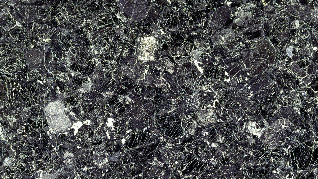 Mörkfärgad stenyta med ljusa ådror och fläckar.