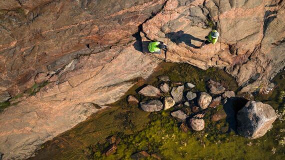Kaksi ihmistä seisoo kalliolla veden äärellä, yllään heijastinliivit ja kypärät.