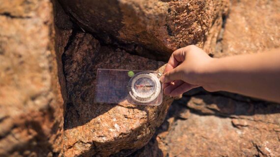 Käsi pitelee kompassia kalliopintaa vasten.