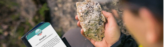 Henkilö pitelee kiveä toisessa kädessä ja puhelinta toisessa kädessä, näytöllä Omakivi-sovellus.