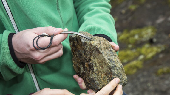 Henkilö raaputtaa kiveä metalliesineellä.