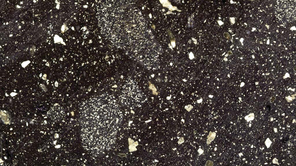 Kuvassa on tumma kivi, jossa on vaaleita pilkkuja ja kiteitä.