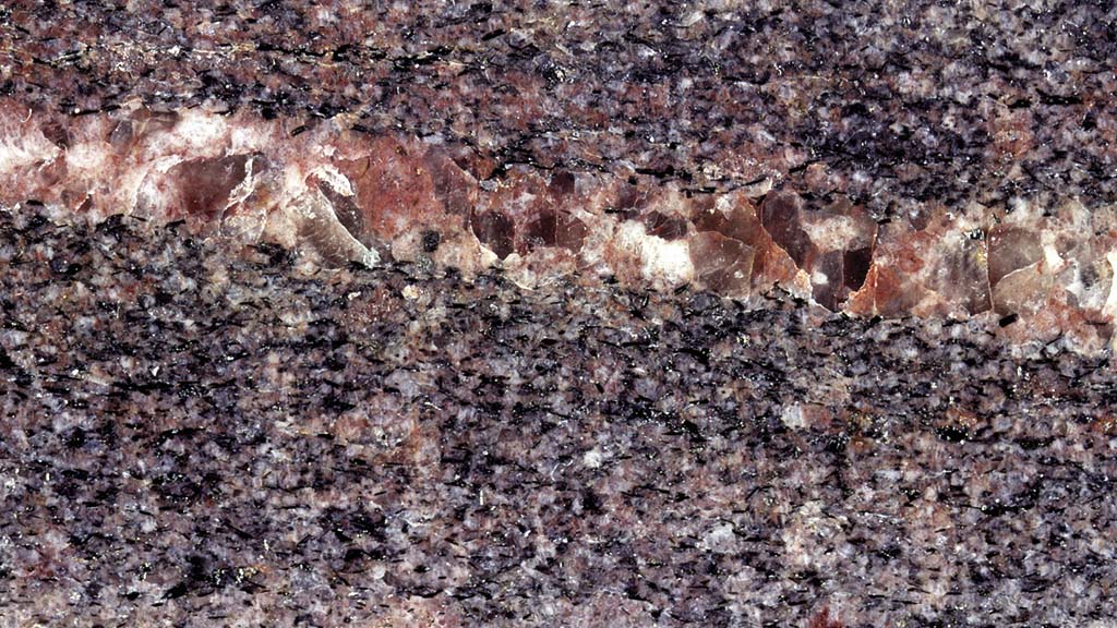 Kuvassa on purppuranvärinen kivi, jossa on poikittainen vaaleanruskea juoni.