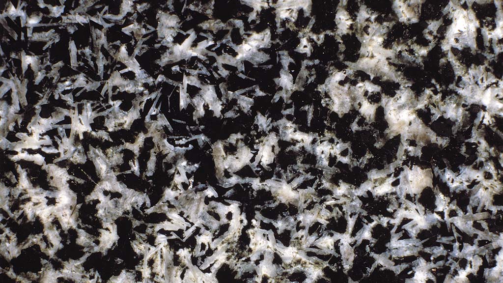 Kuvassa on kivi, jossa on valkoisia neulasmaisia kiteitä mustalla taustalla.