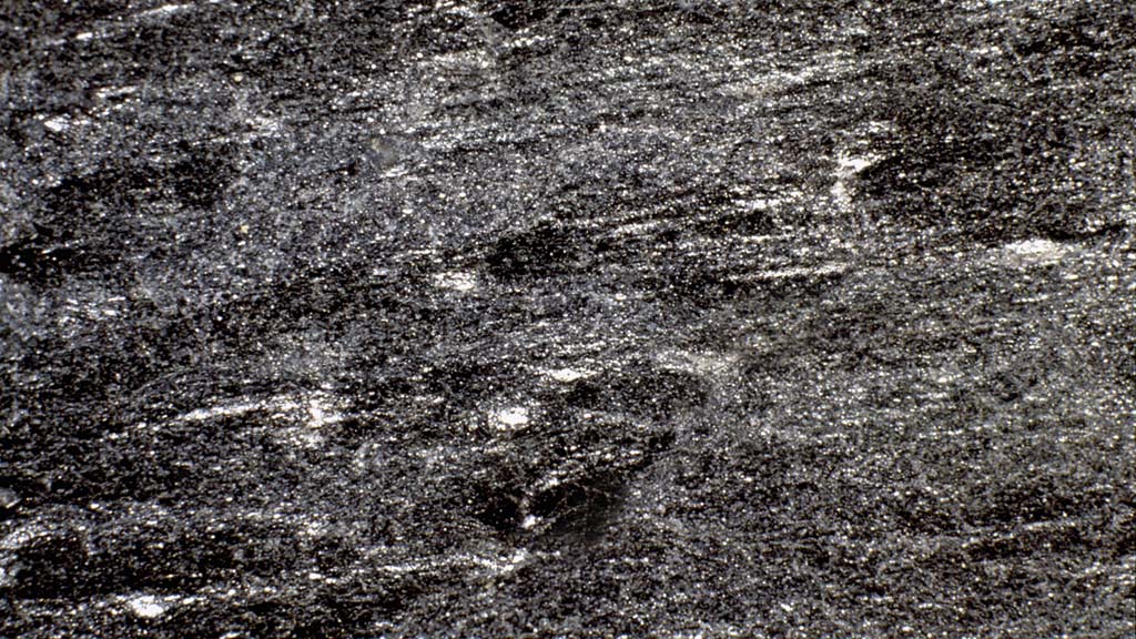 Kuvassa on tummanharmaa kivi, jossa on vaakasuuntaisia juovia.
