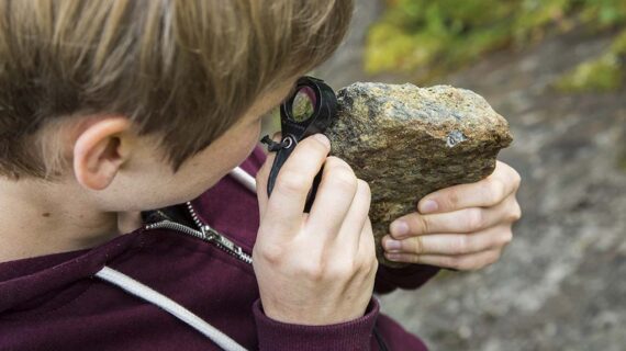 Henkilö tarkastelee kiveä luupin avulla.