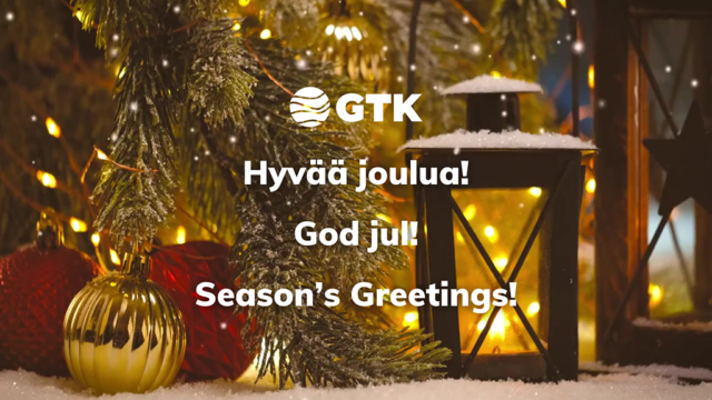 Jouluasetelma, jossa on kuusen oksia, joulupalloja, lyhty ja valoja. Kuvassa lukee "GTK Hyvää joulua! God jul! Season's Greetings!"