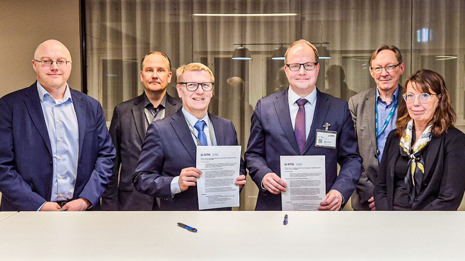 Kuusi henkilöä seisoo rivissä sisätiloissa. Kaksi keskellä olevaa henkilöä pitelee asiakirjoja.