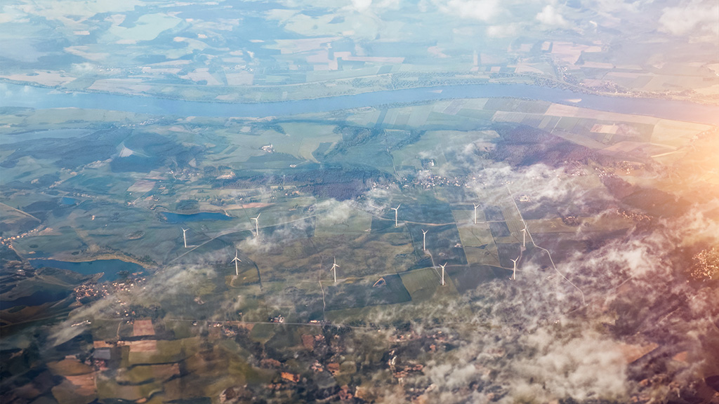 Aerial view of fields and wind turbines, clouds over the landscape.