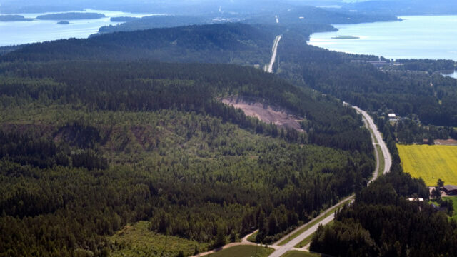 Ilmakuva kesäisestä maisemasta, jossa vihreää metsää, teitä, sorakuoppa ja peltoja. Harjumuodostelma kulkee kuvan keskellä jatkuen järvien ympäröimänä horisonttiin.