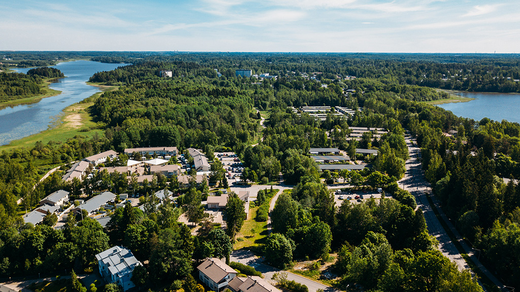 Ilmakuva vehreästä lähiöstä kahden vesistön välissä; metsää, matalia rakennuksia ja tieverkostoja.