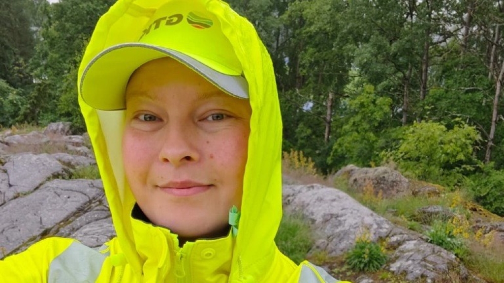Henkilö hymyilee kameralle keltaisissa huomiovaatteissa GTK-lippis päässä.