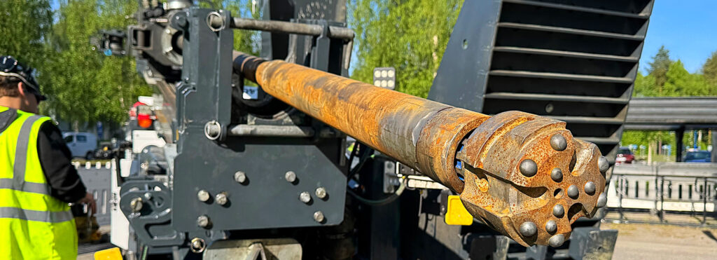 Porauslaite ja huomioliiviin pukeutunut työntekijä ulkona energiakaivon porauskohteessa.