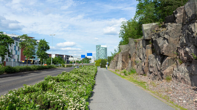 Katu, pyörätie, kallioseinämä ja rakennuksia kaupunkialueella.