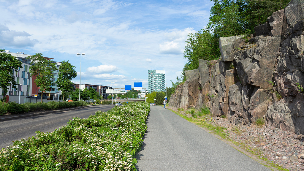 Katu, pyörätie, kallioseinämä ja rakennuksia kaupunkialueella.