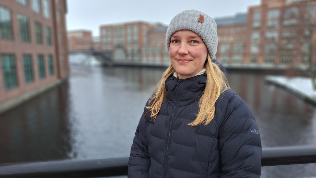 Nainen katsoo hymyillen kameraan, taustallaTammerkoski.