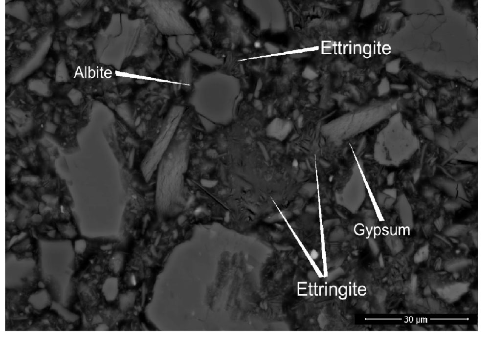 Näyte kovettuvasta kaivostäytöstä, jossa käytettiin ainoastaan sementtiä sideaineena (R4). Ettringiitti täyttää perusmassan välit ja kasvaa mineraalien, kuten albiitin, rajapintoja pitkin. Kuva: Akseli Torppa/GTK.