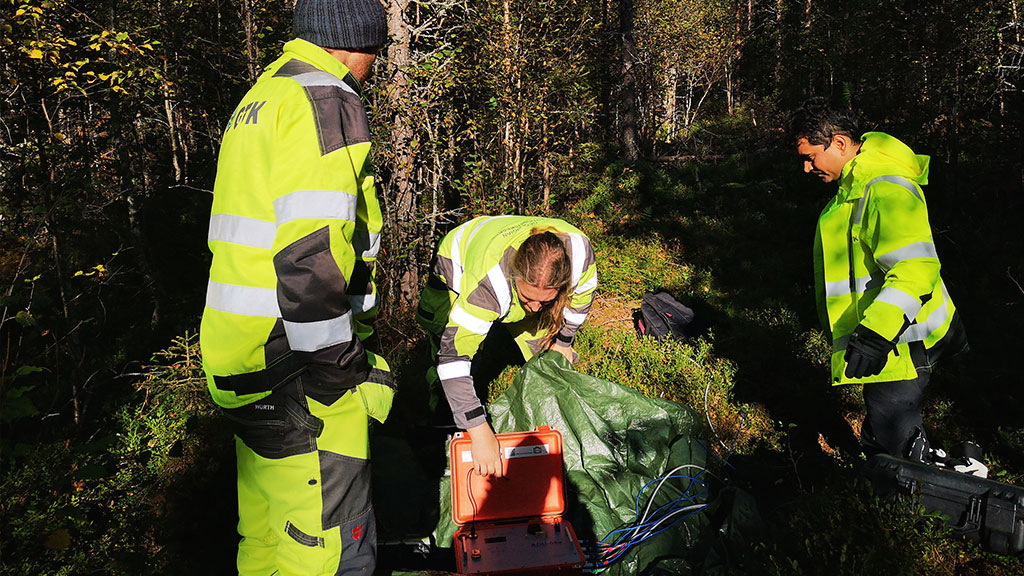 Kolme henkilöä maastossa käyttämässä elektromagneettista laitetta