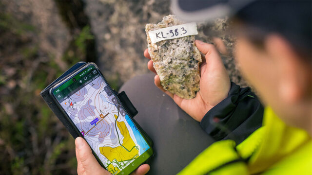 geologist holds a sample and a phone in her hand.