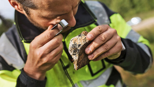 A person looks at a rock sample with a magnifying glass
