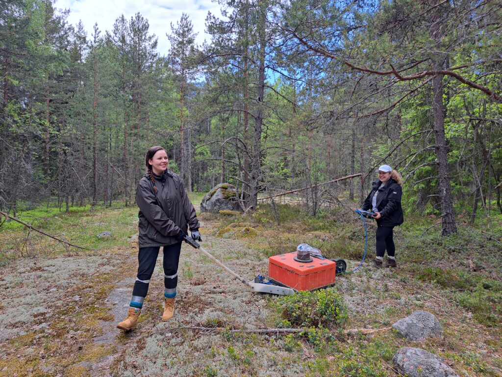 Kaksi henkilöä liikuttaa maastotutkakonetta.