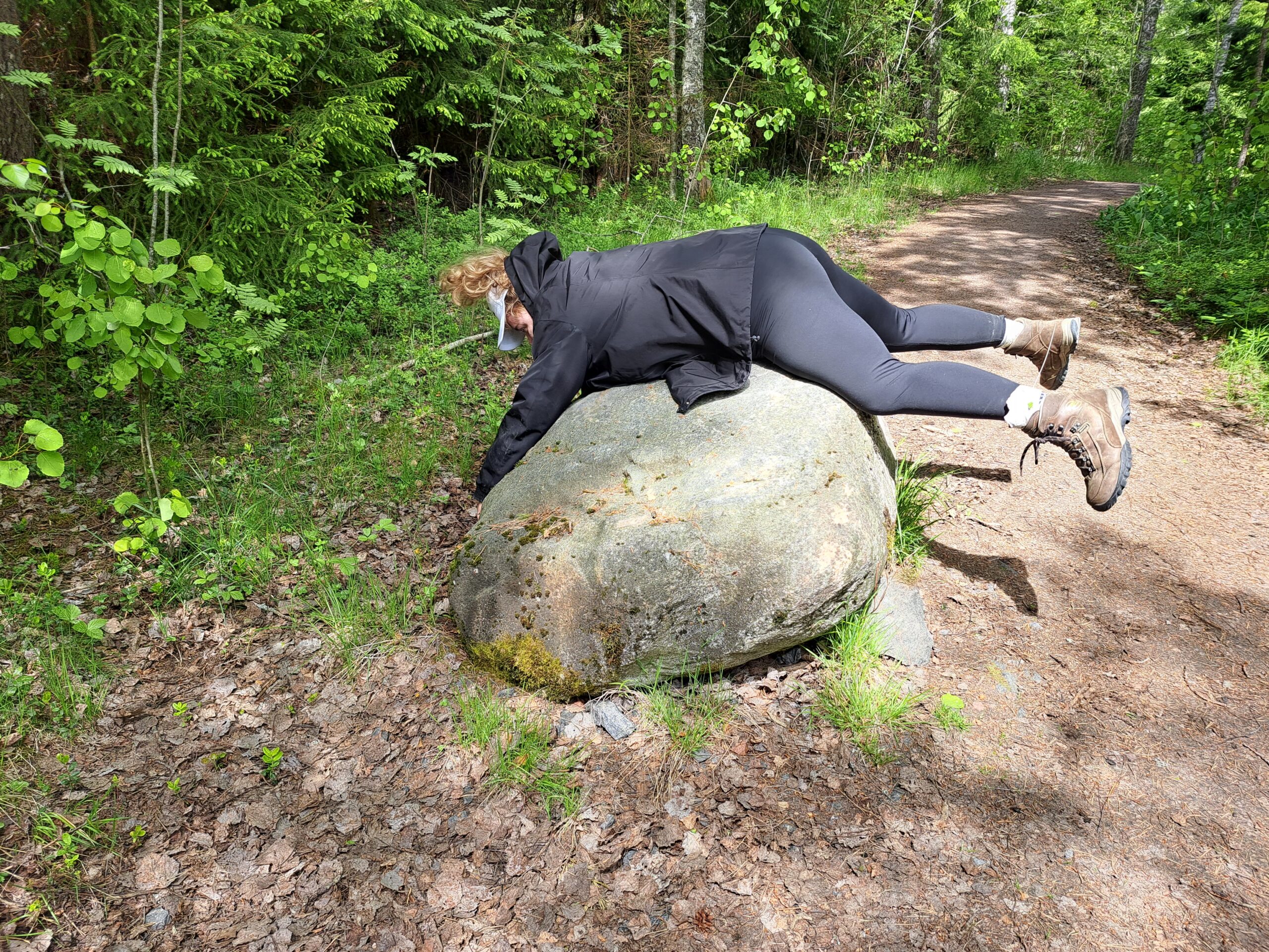 Henkilö mustissa vaatteissa makaa mahallaan kivenlohkareen päällä.