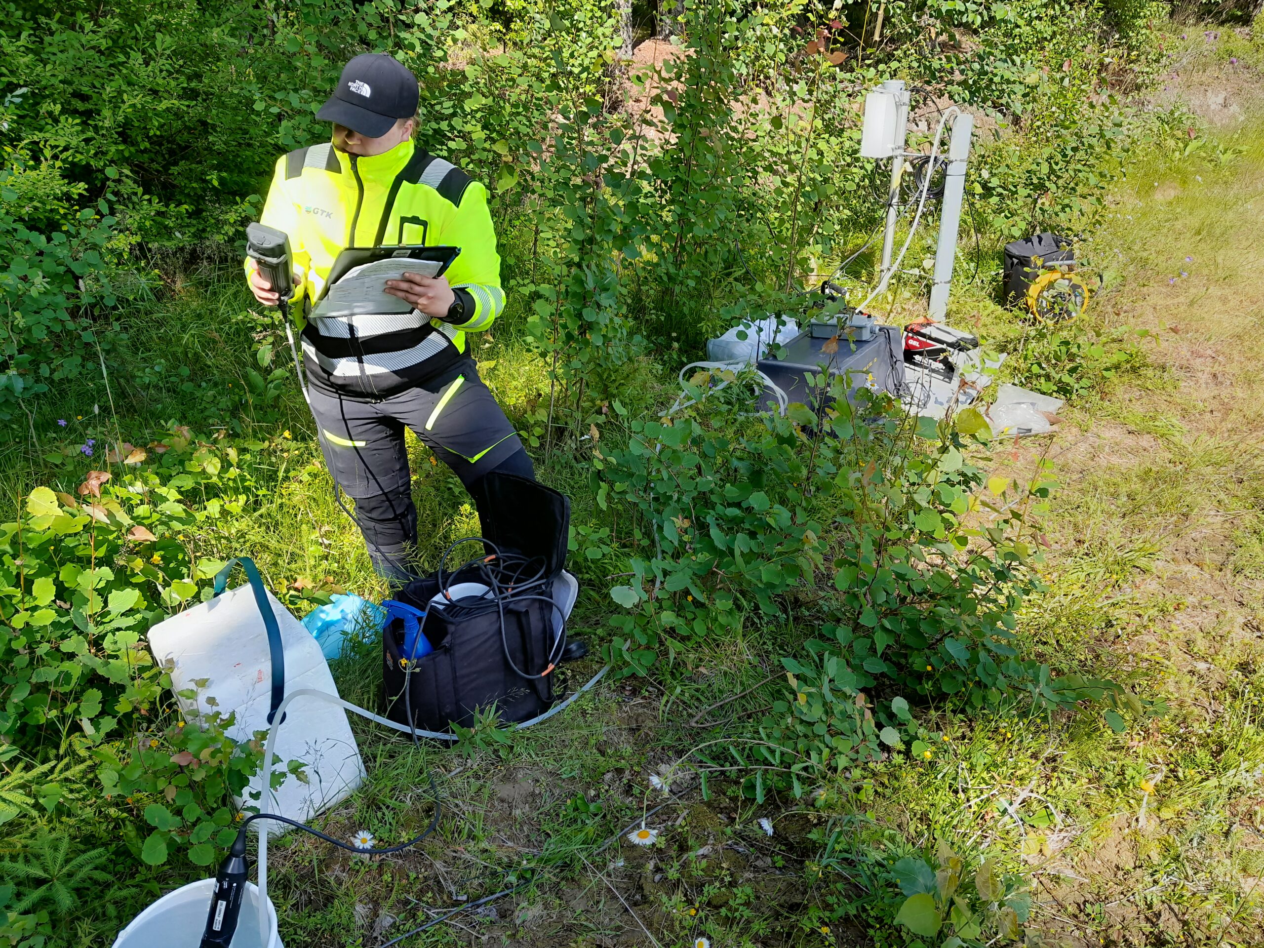 Henkilö huomiovaatteissa metsässä pohjavesinäytteeonottotarvikkeiden kanssa