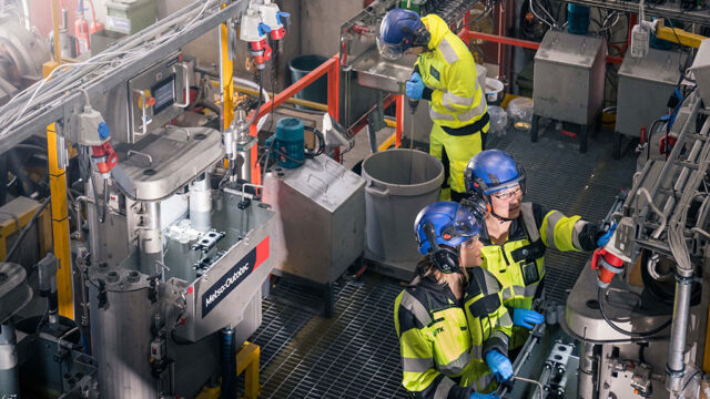 Three workers in a factory. Two are looking together one part of the processa and one is whisking material in a big bowl.