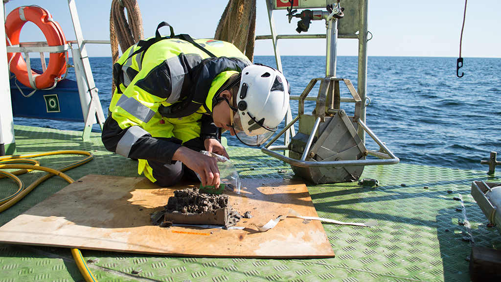 Geologi merellä tutkimusaluksen kannella tutkimassa merenpohjan sedimenttinäytettä.