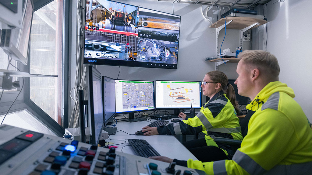 Kaksi henkilöä koetehtaan valvomossa. He katsovat näyttöjä.