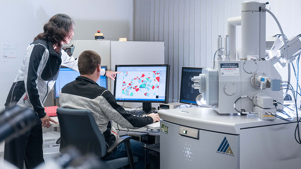 Kaksi henkilöä työskentelevät laboratoriolaitteella. Katsovat näyttöä.