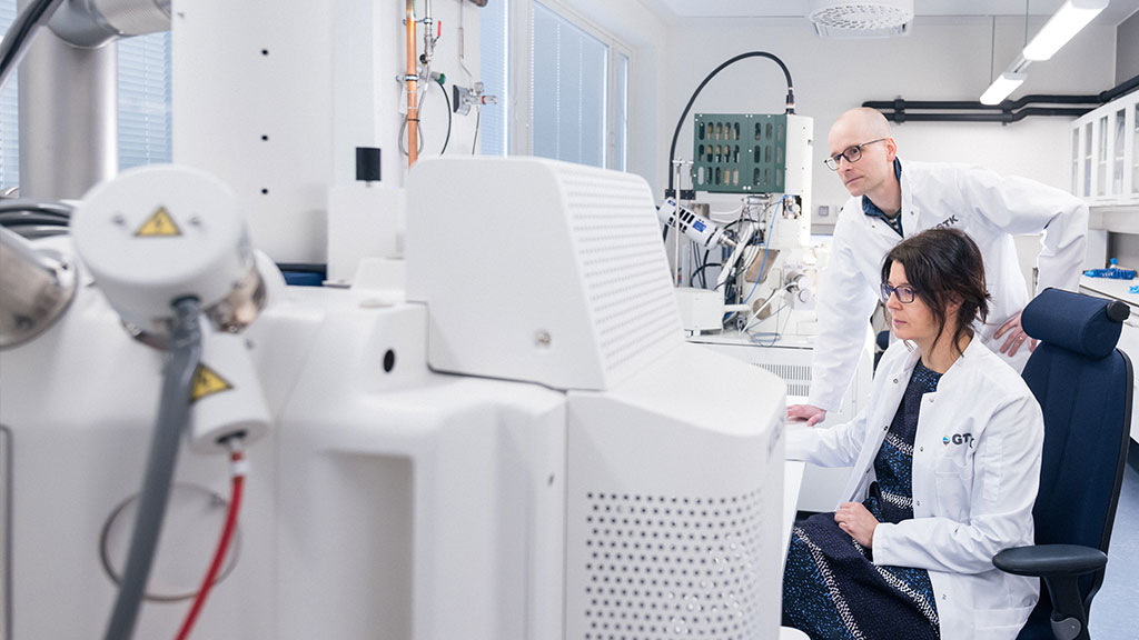2 henkilöä työskentelvät laboratoriolaitteen kanssa. Etualalla itse laite.