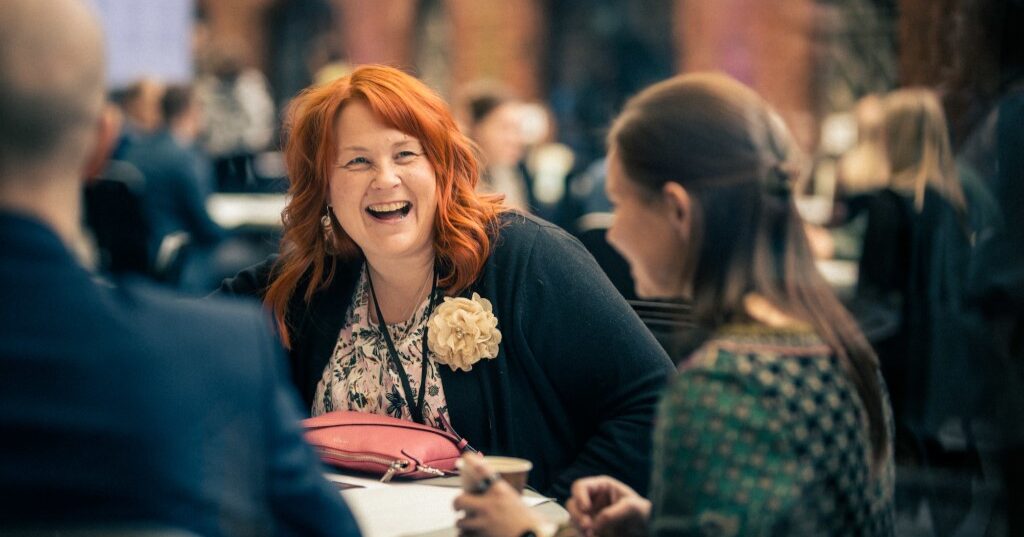 Red-haired woman sits by a table and laughs.